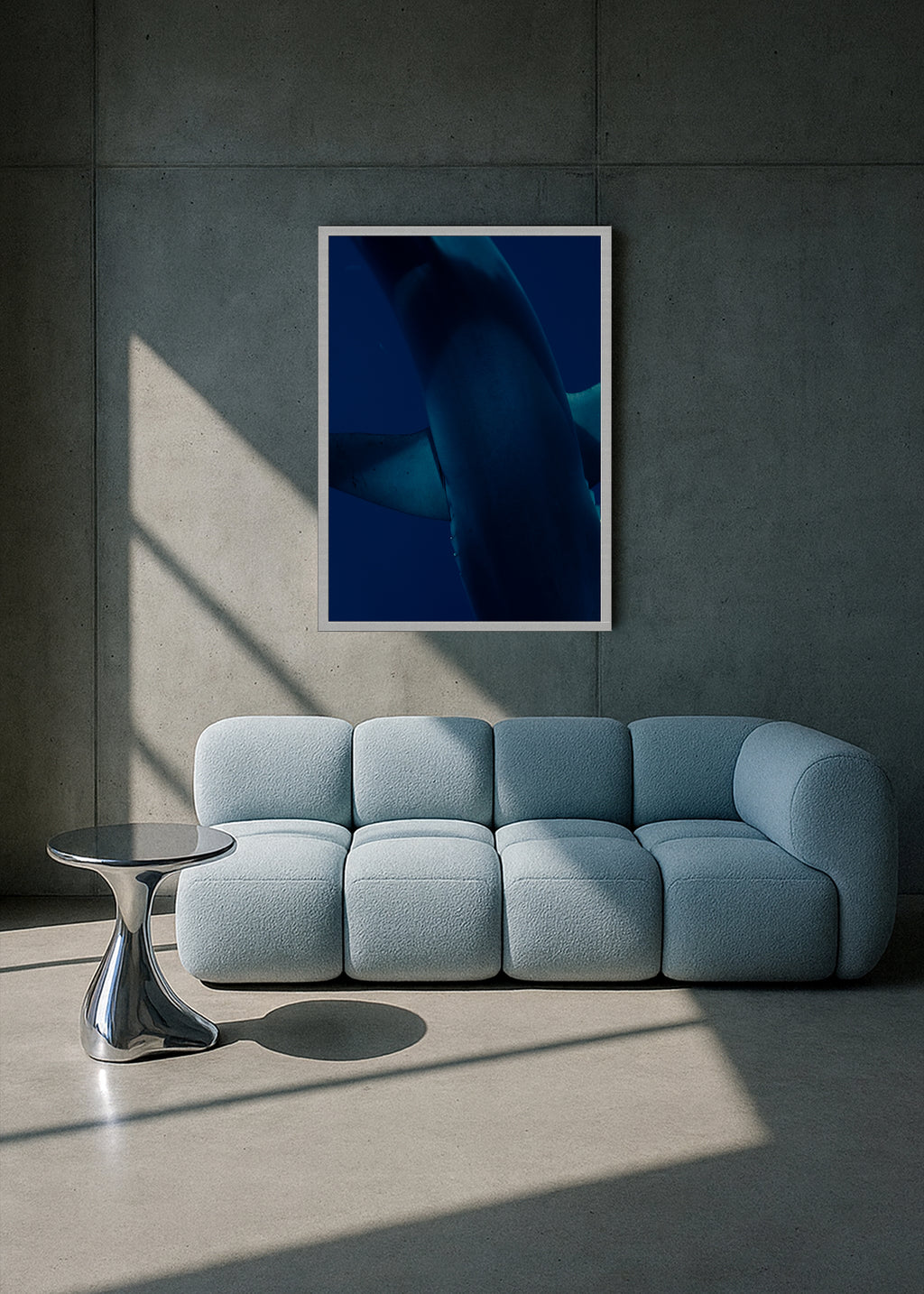 Modern living room with a light blue sofa, round silver table, and abstract blue artwork on a gray wall.
